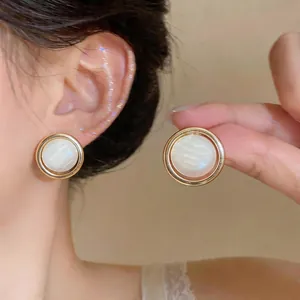 Close-up of French minimalist gold round stud earrings with white pearlescent centers