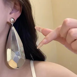 Primer plano de un gran pendiente de gota plateado brillante puesto en la oreja