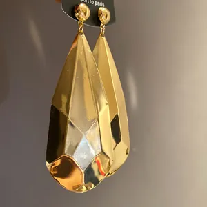 Primer plano de pendientes de gota de metal dorado facetado con acabado brillante