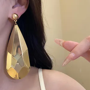 Primer plano de un pendiente de gota facetado dorado de gran tamaño para mujer