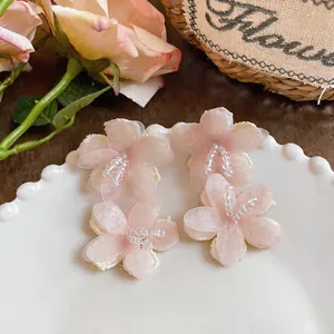 Macro view of pink chiffon flower earrings with clear glass bead centers on white plate.