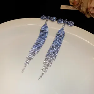Close-up detail of elegant bowknot tassel earrings with sparkling rhinestones on a plate.