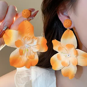 Close-up detail of oversized orange raffia and cloth flower earrings for a vacation look