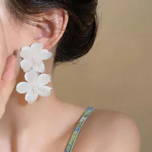 Detail view of elegant white chiffon flower earrings with glass beads on model