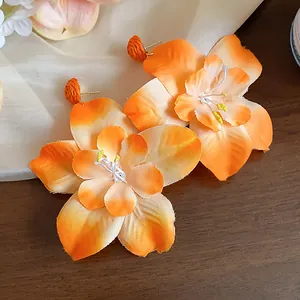 Close-up shot of vibrant orange fabric flower stud earrings with raffia detail accents