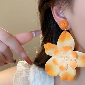 Macro view of a large orange gradient fabric flower earring with woven raffia stud detail