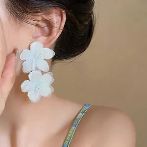 Detail view of elegant white chiffon flower earrings with delicate bead centers on model
