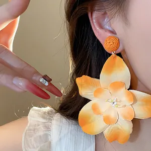 Detailed view of a woman wearing a large orange raffia fabric flower stud earring