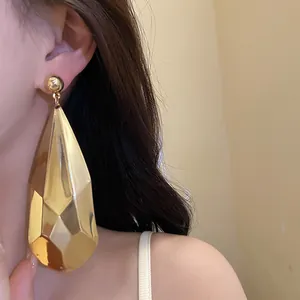 Primer plano detallado de un gran pendiente de gota dorado con facetas en la oreja