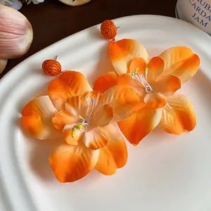 Detailed macro view of orange raffia fabric flower earrings on a white ceramic plate