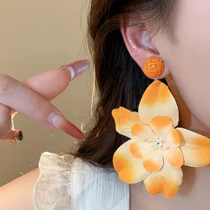 Close-up detail of oversized orange raffia fabric flower earring worn on a model's ear