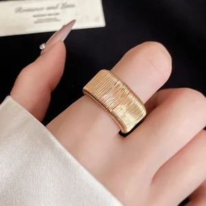 Detailed view of a wide gold wire-wrapped open ring worn on an index finger with a satin sleeve background