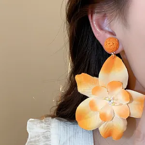 Close-up detail of vibrant orange fabric flower earrings with woven raffia stud.
