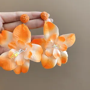 Detail of orange fabric flower earrings with woven raffia studs for a resort look.