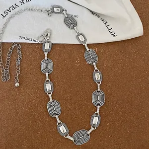 Close-up of vintage silver ethnic waist chain with embossed metal links on cork background.