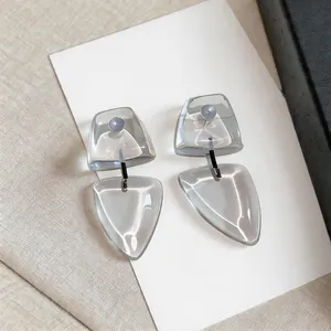 Detalle de pendientes colgantes geométricos de resina gris con pines de plata en tarjeta
