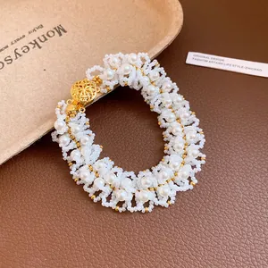 Macro detail of handmade white pearl and bead necklace featuring elegant gold floral clasp