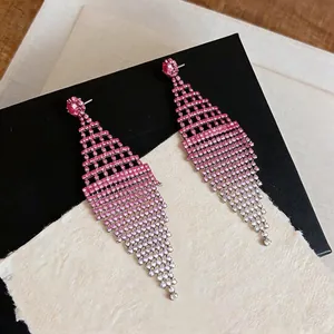Dettaglio di orecchini pendenti con strass sfumati rosa e design a rombo vuoto.