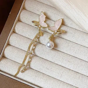 Detailed view of asymmetrical butterfly earrings with pink stones and pearl drops