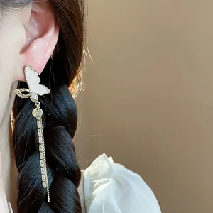 Close-up of elegant gold butterfly dangling earring with white shell and crystal detail