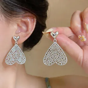 Detailaufnahme der silbernen hohlen Herzohrringe mit Mesh-Design am Ohr.