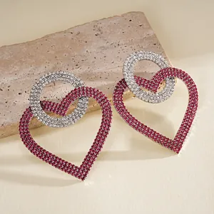 Detalle de elegantes pendientes de corazón geométricos con pedrería magenta y plata