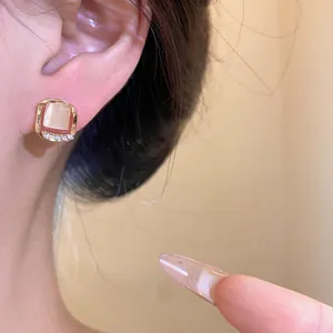 Macro view of square gold-toned stud earring with cat-eye stone and rhinestones on ear