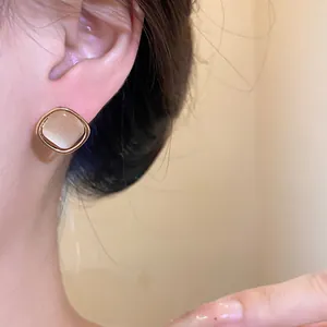 Close-up of elegant square cat's eye stud earring on ear with gold-tone border