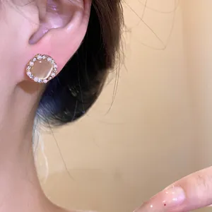 Close-up detail showing an elegant cat's eye stud earring with rhinestone and pearl halo