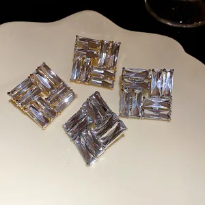 Dettaglio macro di orecchini quadrati con cristalli rettangolari trasparenti oro.