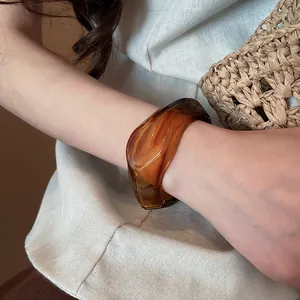 Dettaglio di un bracciale rigido in resina ambrata con design largo e irregolare