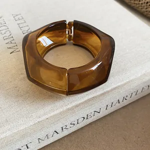 Primo piano di un bracciale rigido geometrico in resina ambrata su sfondo di libro