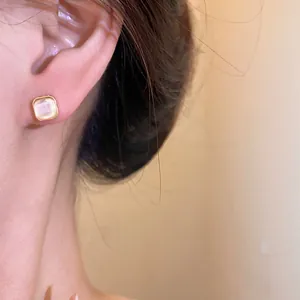 Close-up detail of elegant square cat's eye stud earring with gold border worn on ear