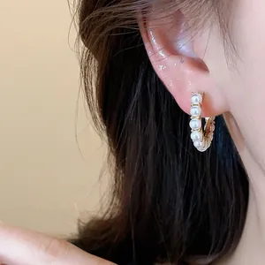 Close-up of 14k gold-plated hoop earrings with small white pearls on a model's ear.