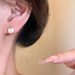 Close-up of square cat's eye stud earring on ear with elegant gold trim detail.
