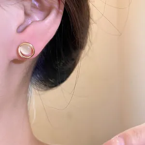 Detailed close-up showing an elegant round cat's eye stud earring with gold frame on ear