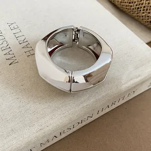 Dettaglio di un bracciale rigido largo in argento irregolare su un libro di lino beige.