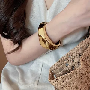 Primo piano di un bracciale rigido irregolare in resina dorata sul polso di una modella