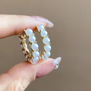 Close-up of elegant 14k gold plated pearl hoop earrings held between fingers for detail.