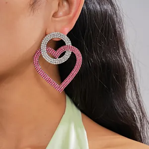 Detalle de pendientes extragrandes con corazón de pedrería rosa y círculo plateado en modelo