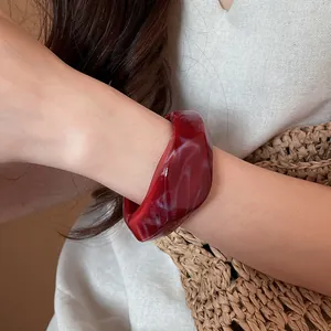 Primo piano di un bracciale in resina rossa con texture marmo bianco sul braccio della modella