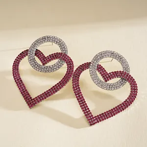 Detalle de pendientes de corazón y círculo entrelazados con cristales rojos y plateados