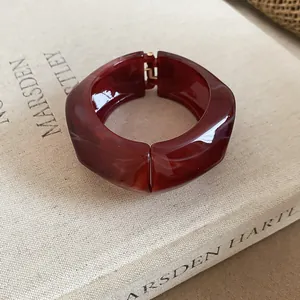 Primo piano di un bracciale rigido in resina rosso ambra con fascia larga e chiusura.