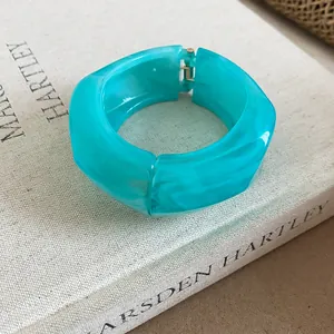 Dettaglio di bracciale in resina turchese con cerniera su un libro di lino