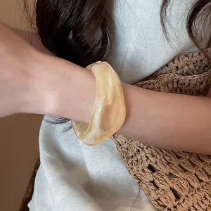 Primo piano di un bracciale rigido in resina crema marmorizzata indossato per un look estivo.