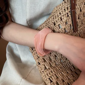 Dettaglio di un bracciale rigido in resina rosa spesso e irregolare indossato sul polso