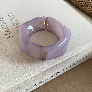 Dettaglio di un grosso bracciale rigido aperto in resina viola dal design geometrico unico.