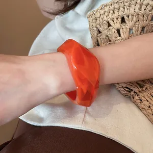 Dettaglio di un bracciale rigido in resina arancione con design geometrico irregolare
