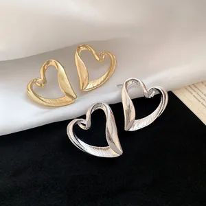 Textured gold and silver heart-shaped stud earrings shown on black and white fabric
