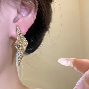 Close-up of elegant gold geometric earrings with zircon inlay worn by model